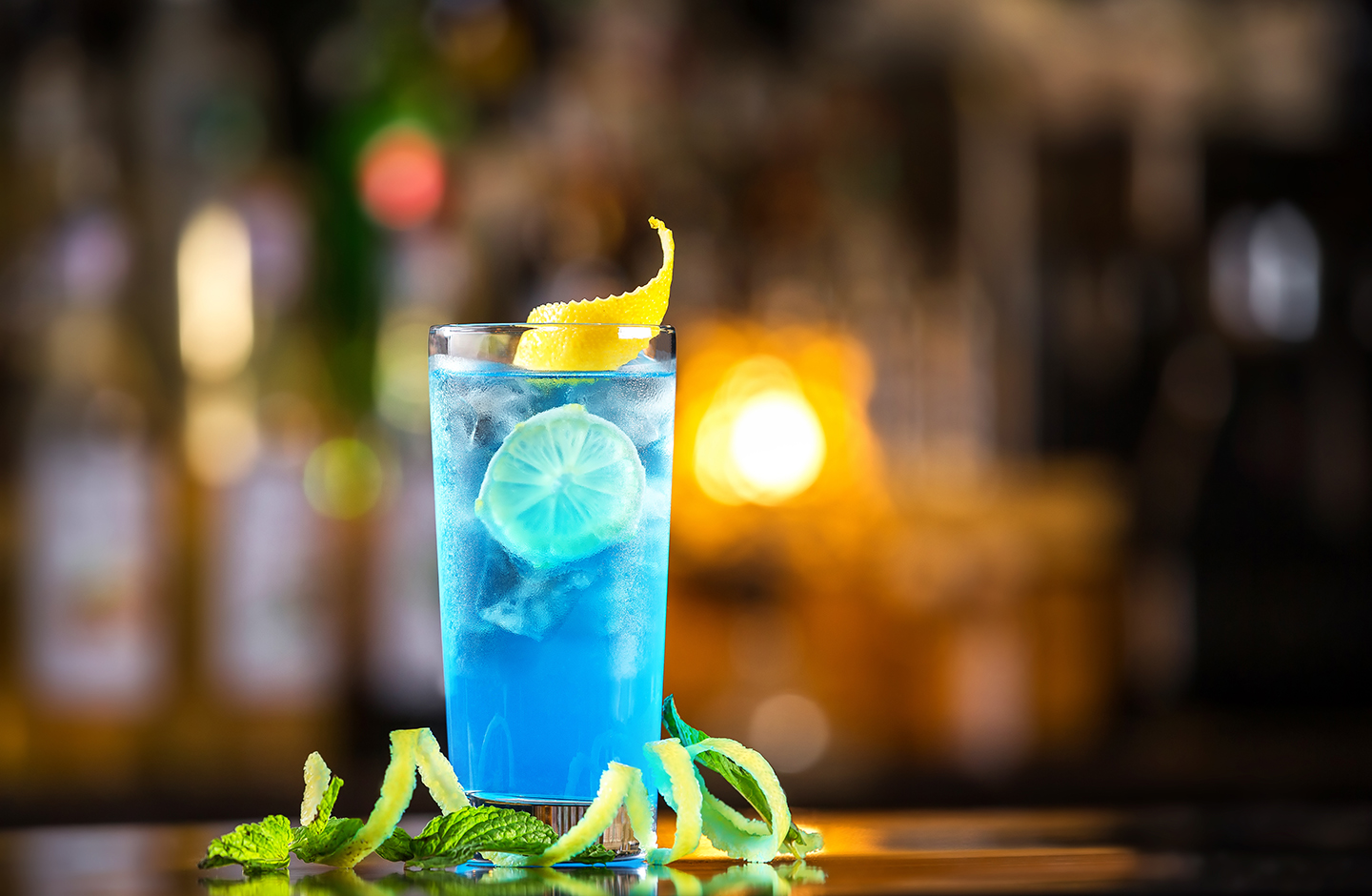 Ein blauer Cocktail mit Dekoration aus Limettenschalen vor einem dunklen, verschwommenen Hintergrund
