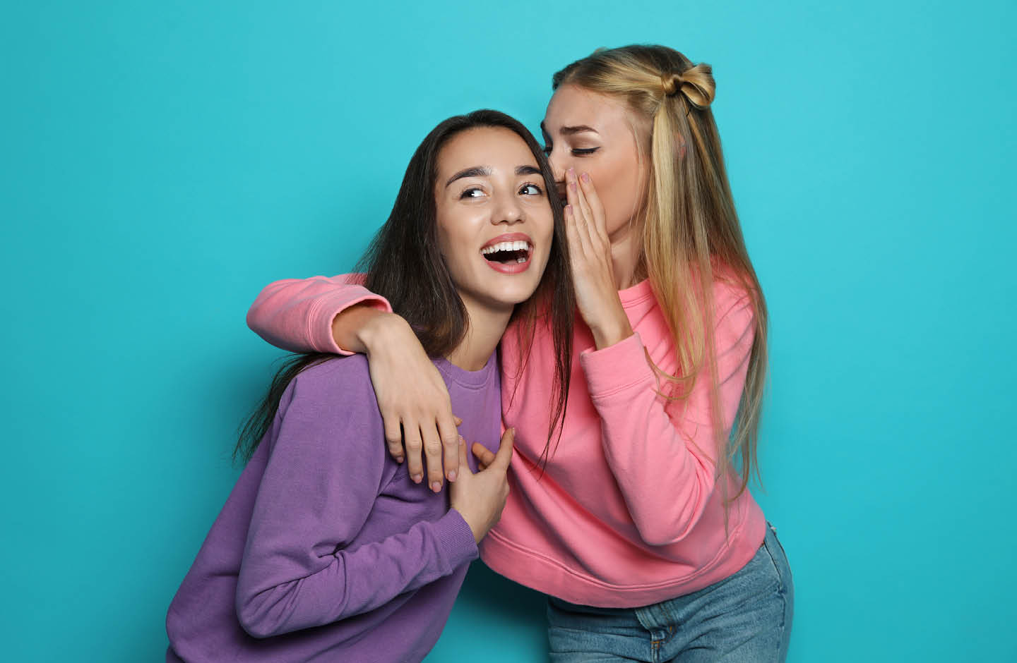 Zwei junge Frauen flüstern sich etwas ins Ohr.